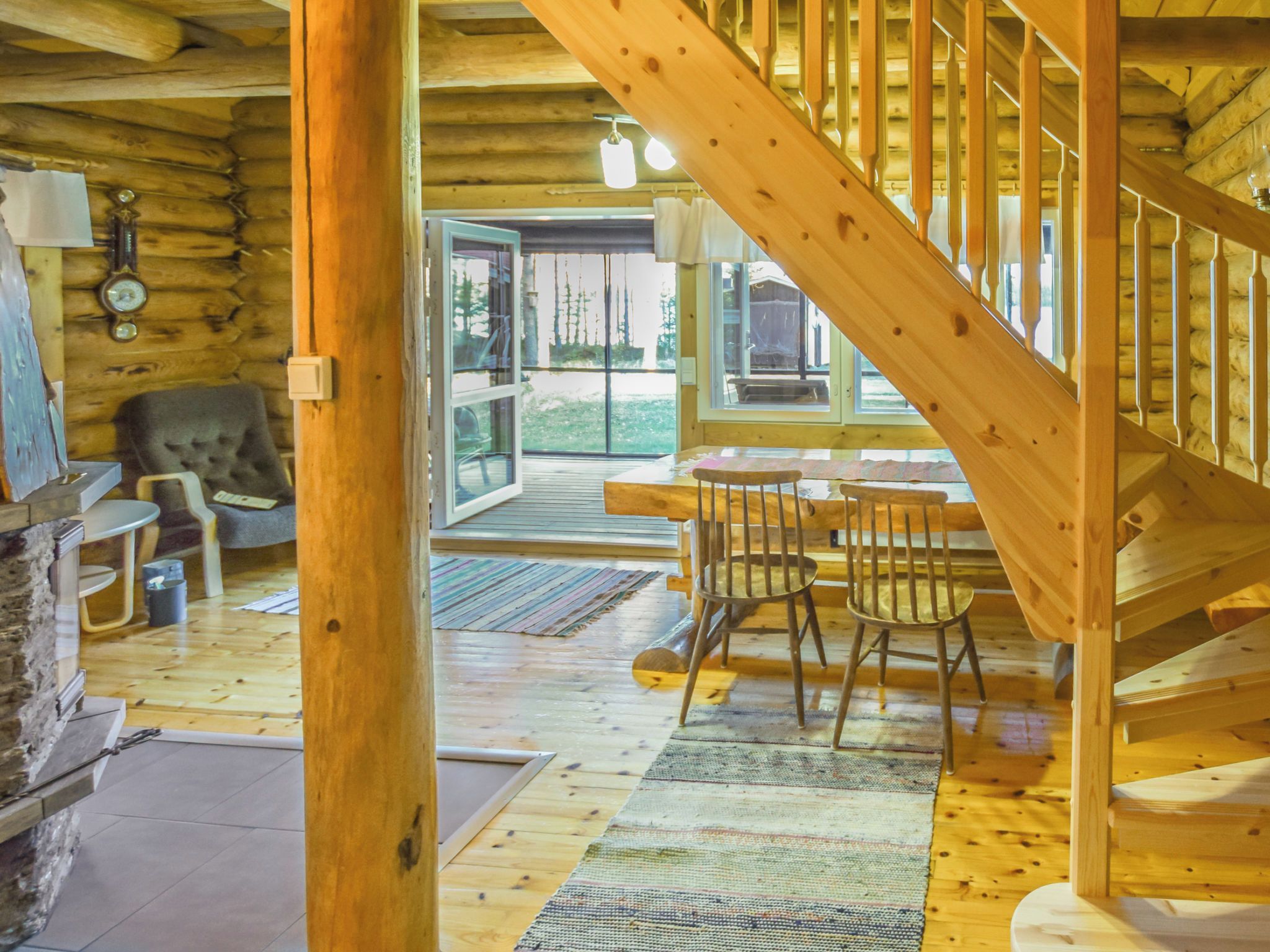 Un intérieur en bois avec un escalier, un coin repas avec des chaises et une vue à travers une porte vitrée.