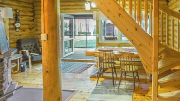 A wooden interior with a staircase, a dining area with chairs, and a view through a glass door.
