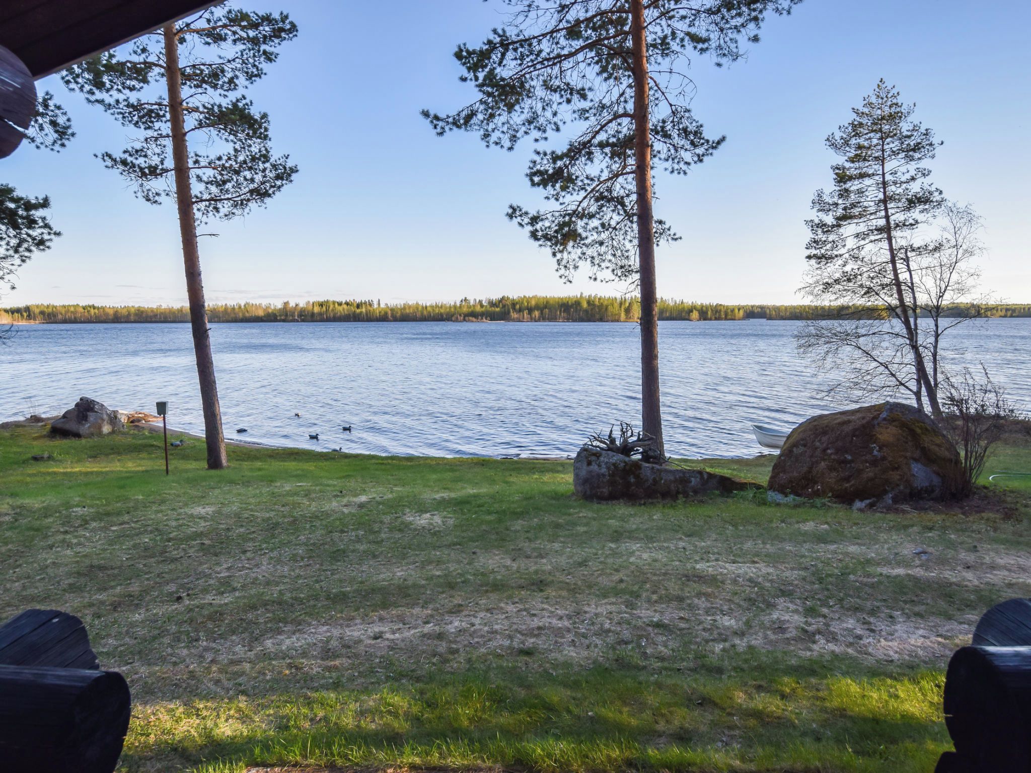 Une vue sur le lac, avec une zone herbeuse, des arbres et un bateau sur l’eau.