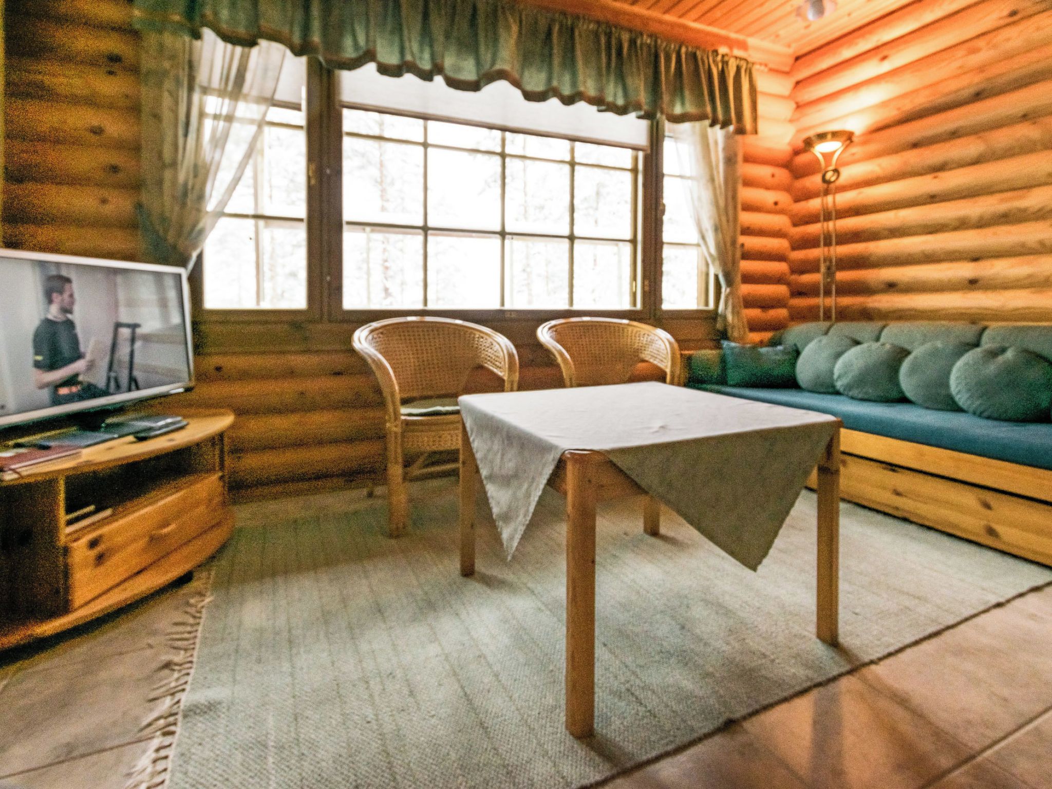 Een gezellig blokhutinterieur met een televisie, twee rieten stoelen, een tafel en een bank.