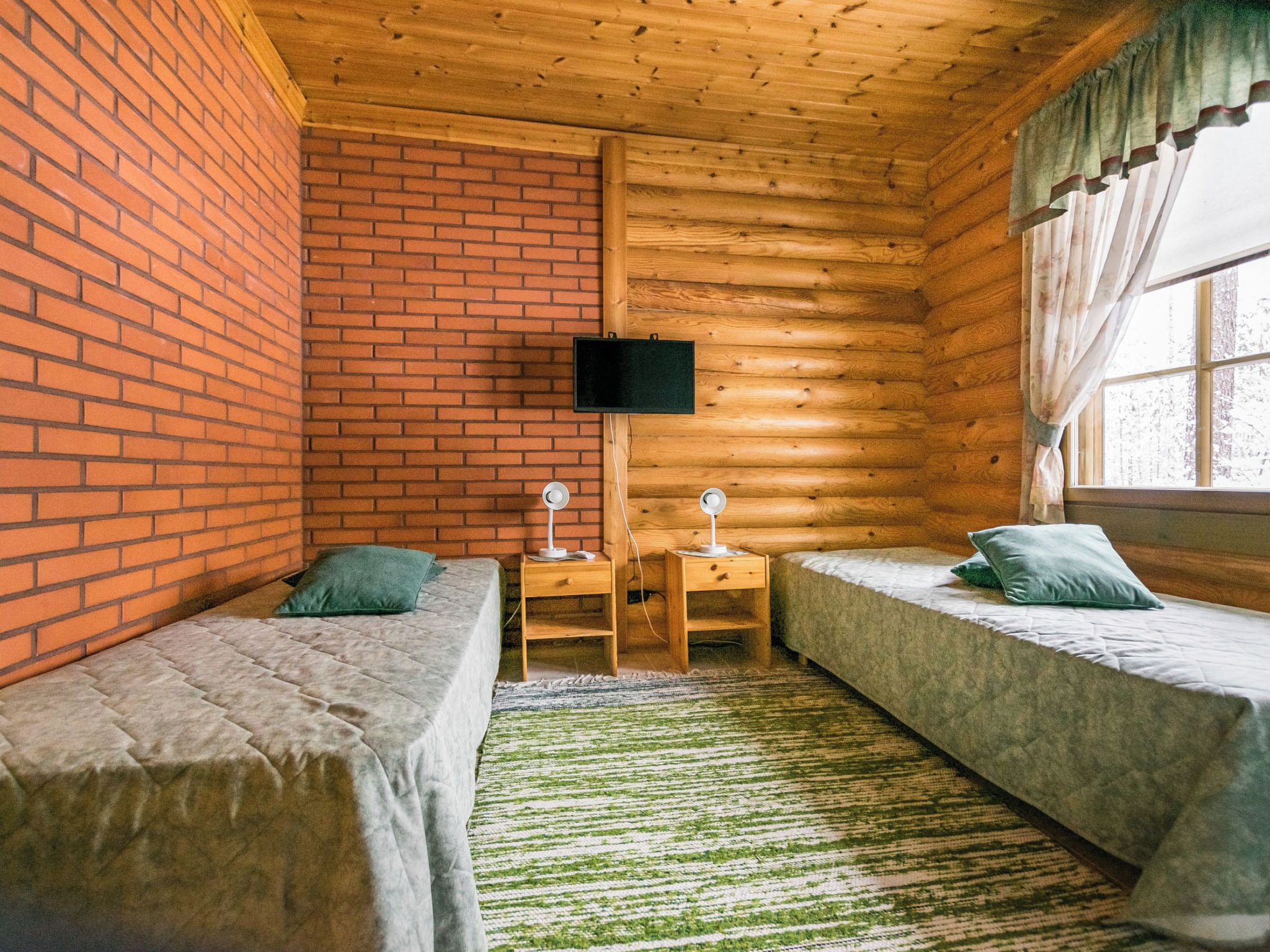 Een kamer met twee bedden, een aan de muur bevestigde televisie en een raam met gordijnen.
