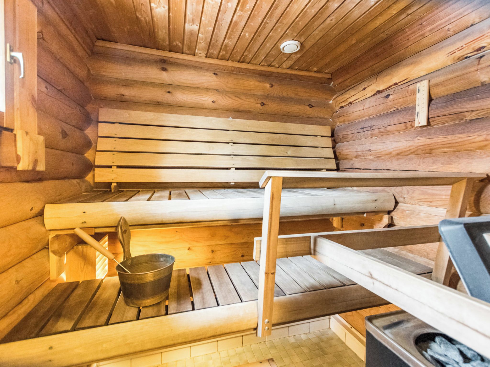A wooden cabin interior with bunk beds, a metal bucket, and a stove.