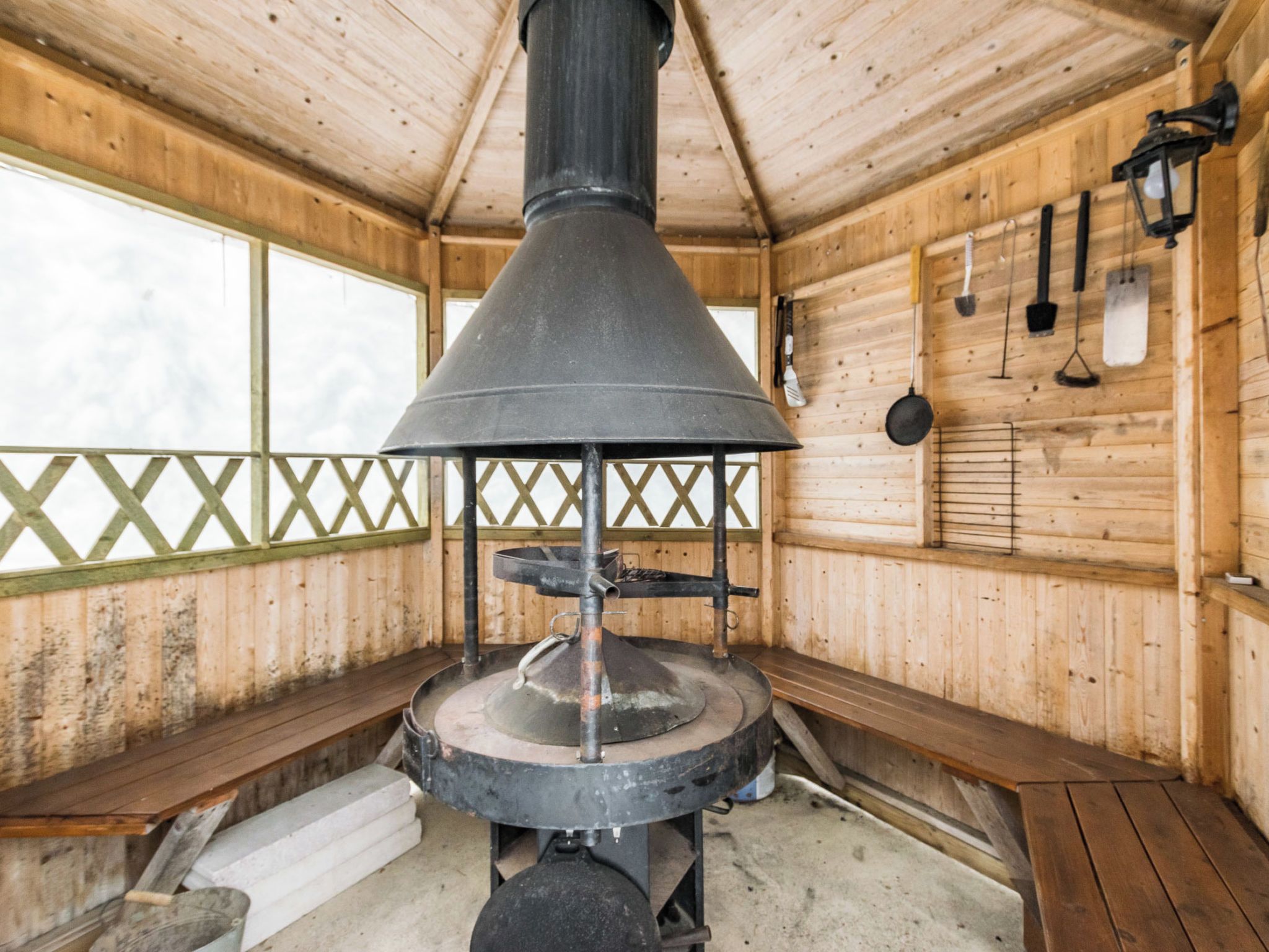 A rustic wooden cabin with a large central stove, wooden benches, and a window with a view.