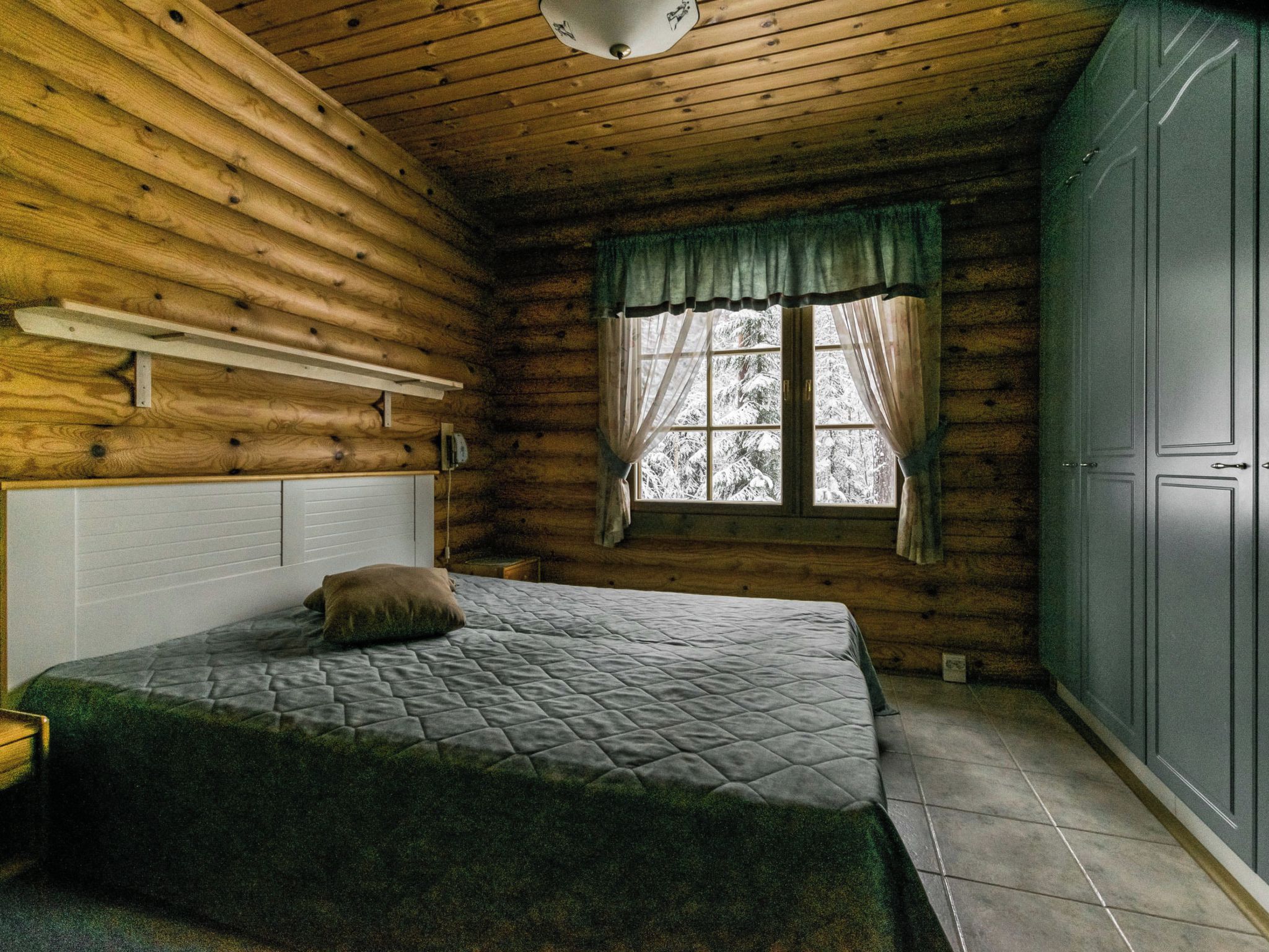 Quarto de cabana de madeira com cama, janela com cortinas e guarda-roupa.