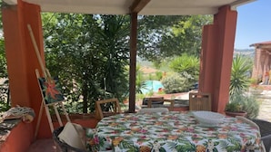 A covered patio with a round table and chairs, surrounded by potted plants and a painting on easels. - Contrada Brecciano by Interhome (Città Sant'Angelo)