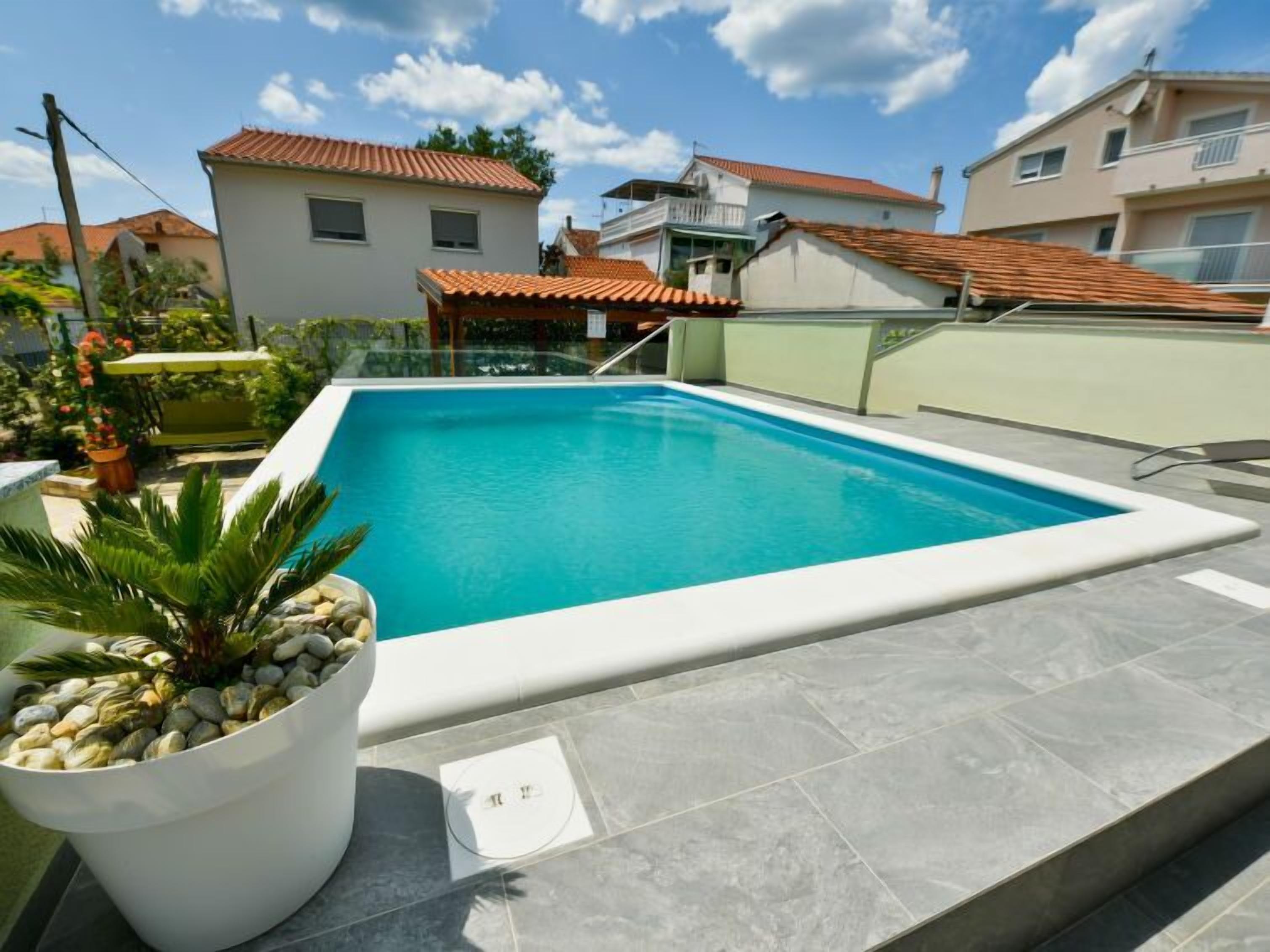 A rectangular swimming pool with a white border, surrounded by grey tiles.