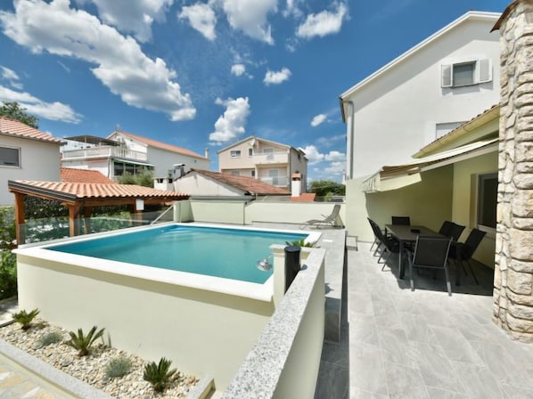 A swimming pool with a patio area, surrounded by a stone wall and a covered seating area.