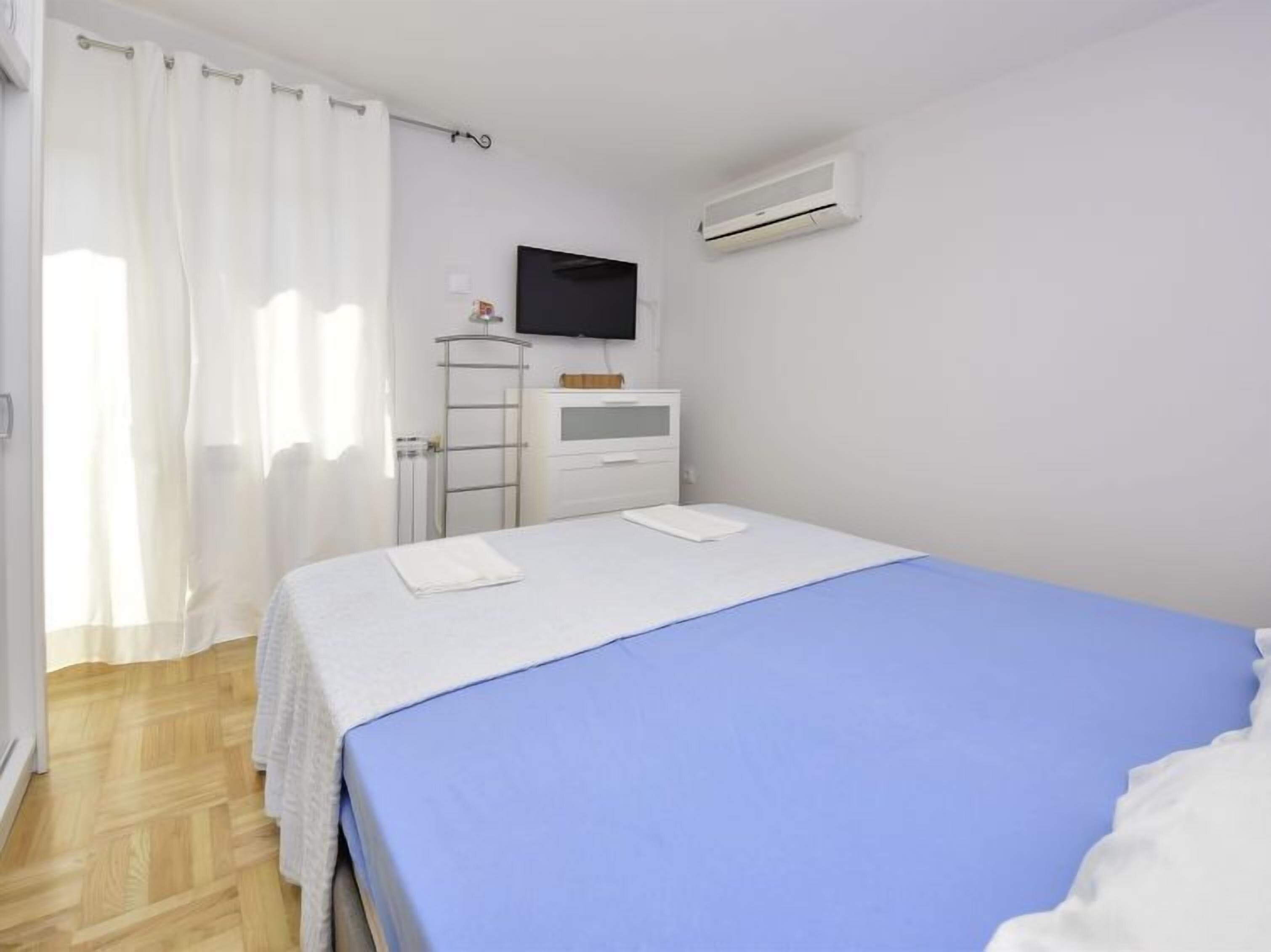Un dormitorio con cama, televisión, aire acondicionado, armario y ventana con cortinas.