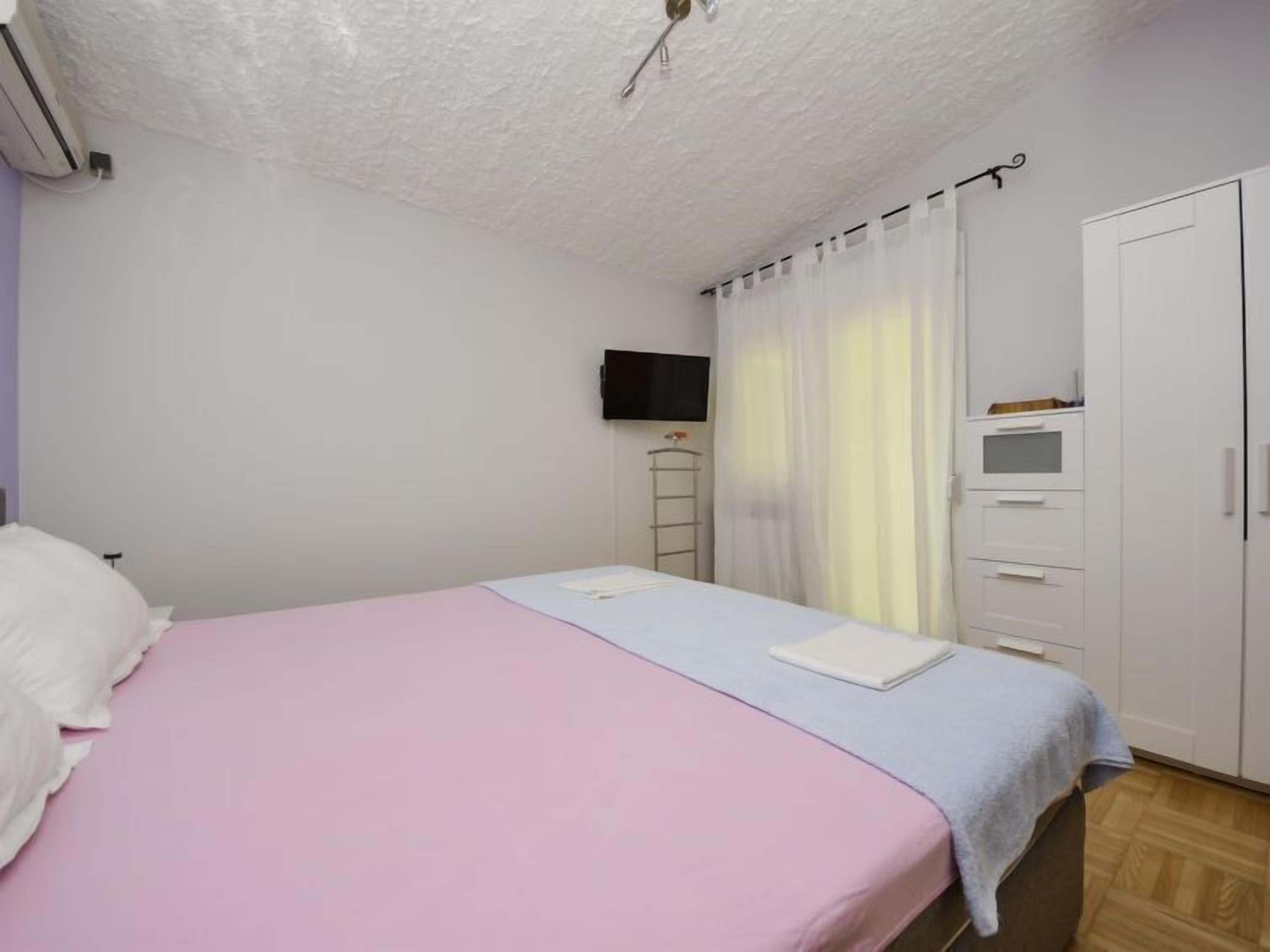 A bedroom with a bed, a TV mounted on the wall, a wardrobe, and a window with curtains.