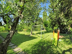 Relax in a serene garden setting with a swing set and play structure surrounded by lush greenery and a meandering stone pathway.