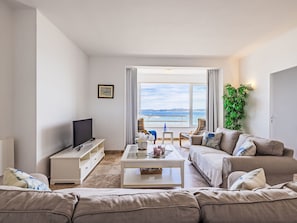 Een moderne woonkamer met een flatscreen televisie, een bank, een salontafel en uitzicht op de zee door grote ramen.