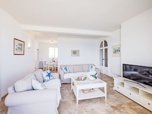 A modern living room with a sofa, coffee table, TV stand, and dining area.