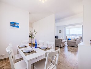 A modern living room with a dining area, white furniture, a view to the outside, and a painting on the wall.