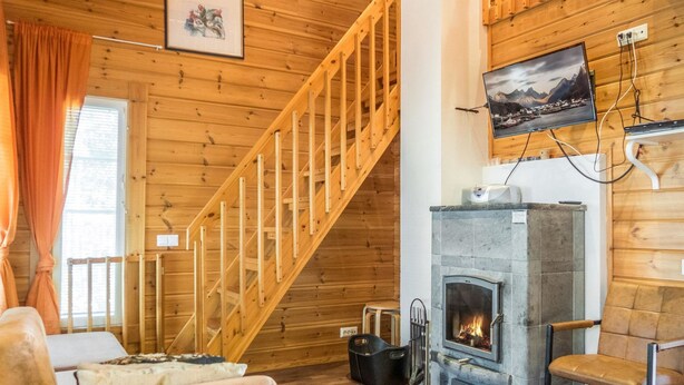 Interior acogedor de una cabaña con una escalera de madera, chimenea, televisor montado en la pared y un espacio de estar confortable.