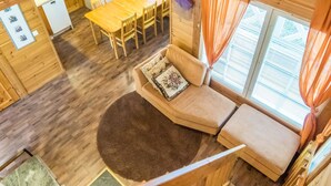 Interior de una cabaña de madera con comedor, sofá y ventana con cortinas.