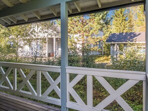 Een overdekt buitengebied met een witte balustrade, een houten terras en uitzicht op woongebouwen en bomen.