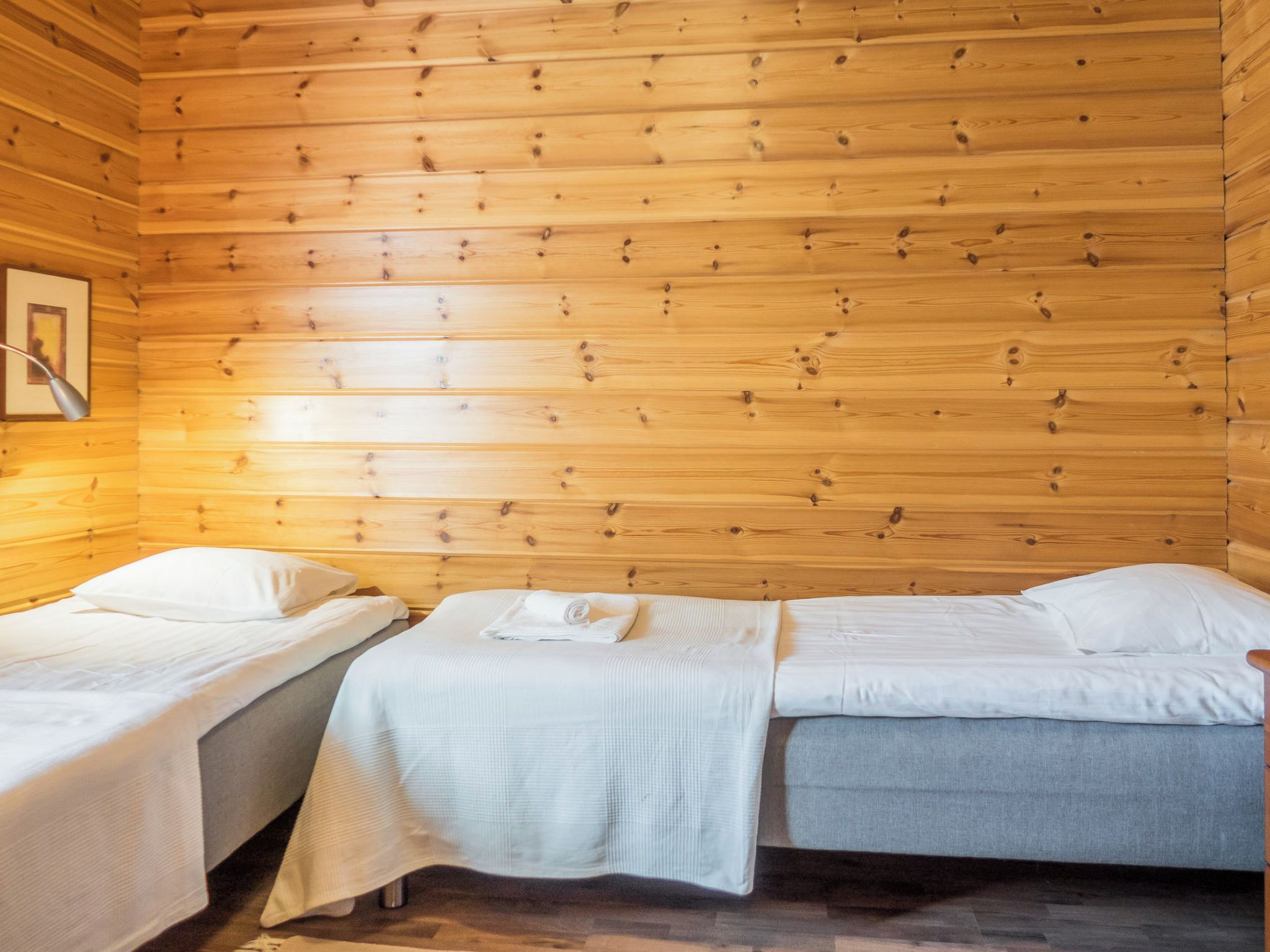 A cabin with two single beds, wooden walls, and a framed picture on the left wall.