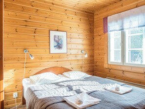 A wooden-paneled room with a bed, two bedside lamps, a window with blinds, and a framed artwork on the wall. - Klz 1. akaatti by Interhome (Sotkamo)