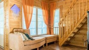 Interior acogedor de una cabaña con escalera de madera, un sofá y una ventana con cortinas.
