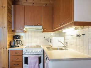 A compact kitchen with wooden cabinets, a built-in microwave, a stove, and a sink. - Klz 1. akaatti by Interhome (Sotkamo)