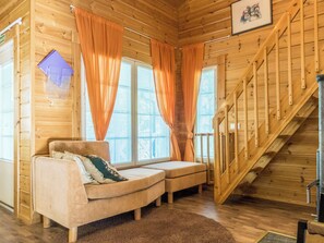 A wooden interior with a sofa, curtains, and a staircase.