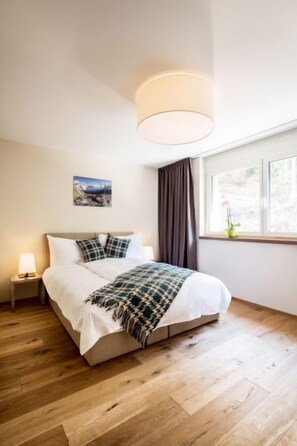 Une chambre à coucher comprenant un lit, une table de chevet, une lampe, une fenêtre avec des rideaux et un tableau accroché au mur.
