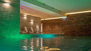 Une piscine intérieure avec un mur en pierre et une rangée de chaises longues.