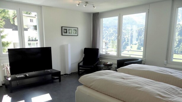 Une chambre d’hôtel moderne dotée d’un grand lit, d’une télévision, d’un bureau et offrant une vue sur une forêt.