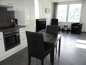 A modern kitchen with white cabinetry, a black stove, and a dining area with a table and chairs. - Barbara Ost Appartement/Fewo 2-Bettwohnung by Interhome (Engelberg)