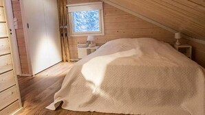 A cozy attic bedroom with a wooden ceiling, a single bed, a small bedside table, and a window with a view of trees.