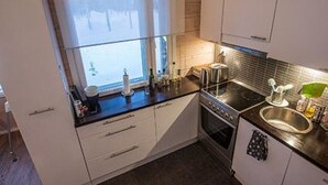 A compact kitchen with white cabinets, a black countertop, a window with frosted glass, and a stainless steel sink.