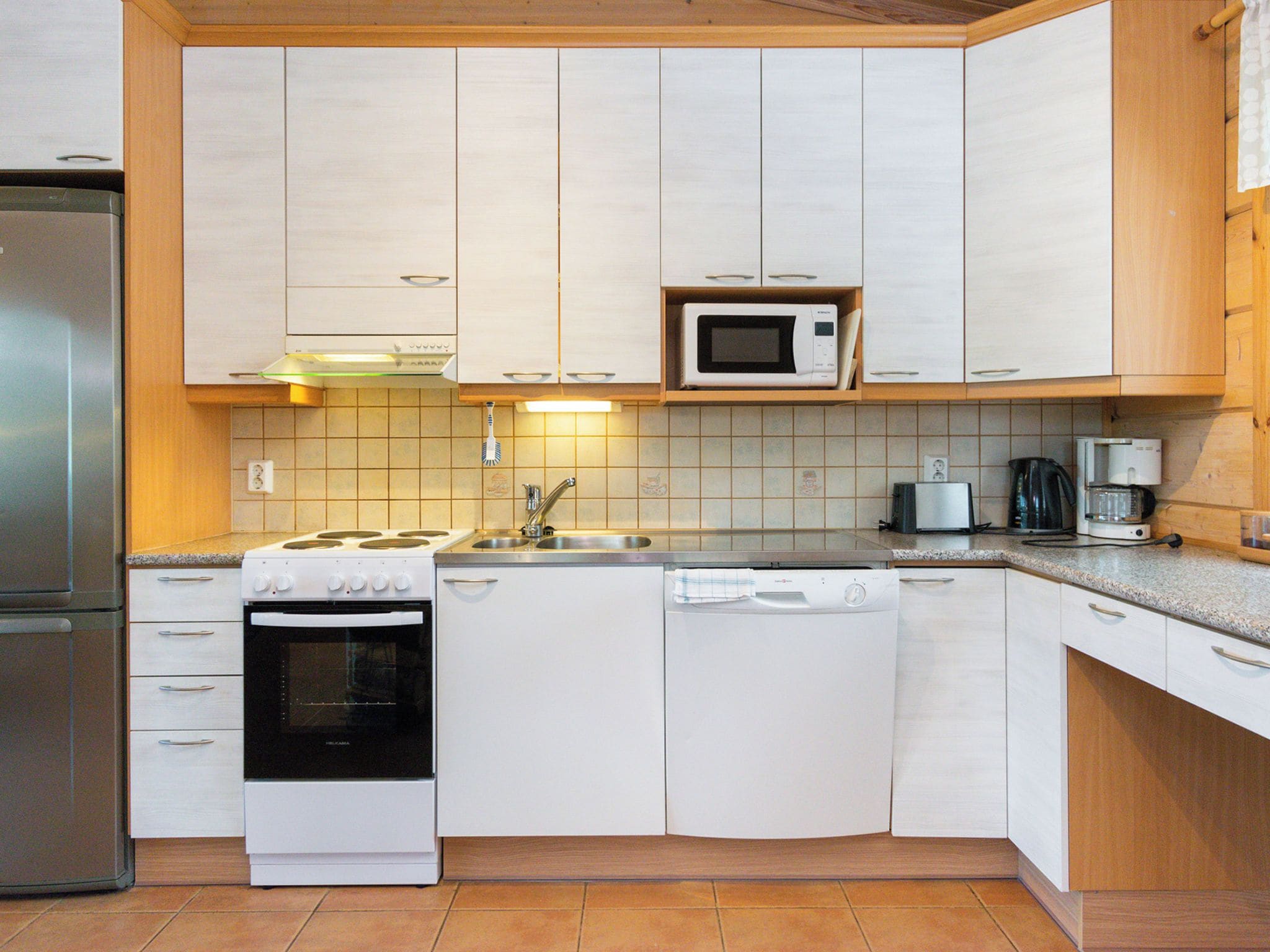 Cocina compacta con armarios blancos, microondas integrado, estufa, lavavajillas y cafetera.