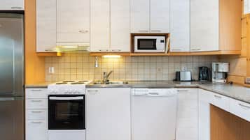 Cocina compacta con armarios blancos, microondas integrado, estufa, lavavajillas y cafetera.