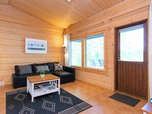 Interior de una cabaña de madera con un sofá, una mesa de centro y una puerta que da al exterior.