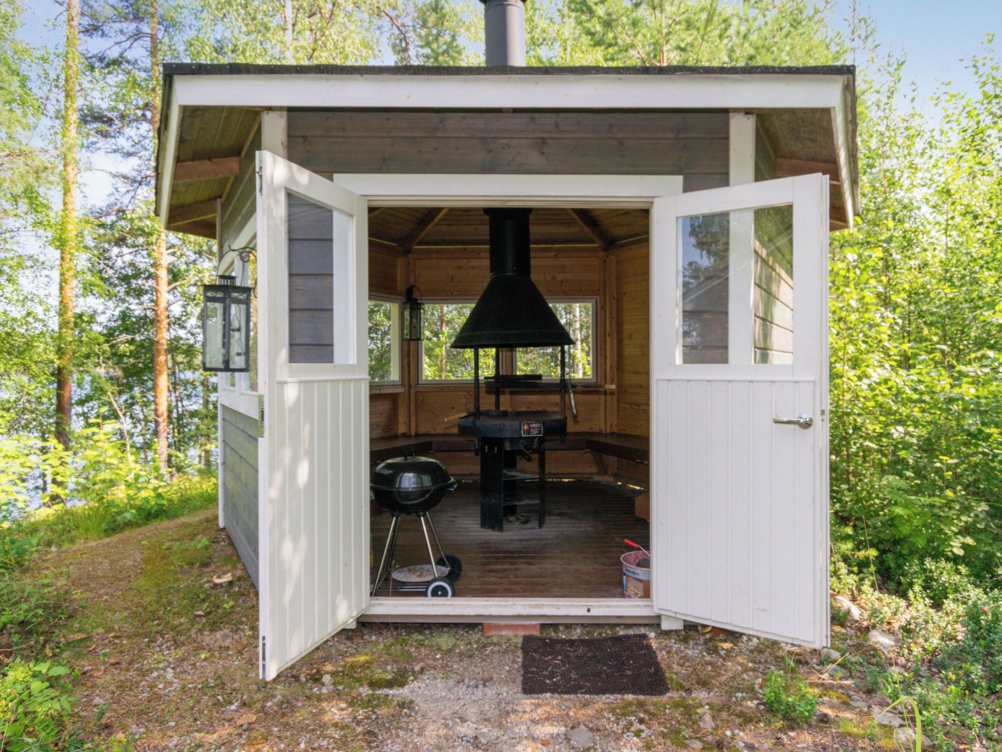 Una cabaña de madera con puerta abierta, una chimenea, una parrilla y un farol.