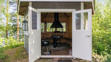 Una cabaña de madera con puerta abierta, una chimenea, una parrilla y un farol.