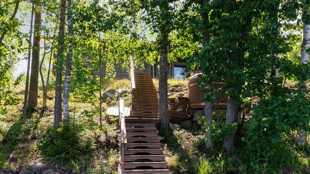 A wooden bridge over a stream in a forested area with trees and a wooden structure in the background.