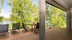 A wooden deck with a table and chairs overlooking a lake, surrounded by trees.