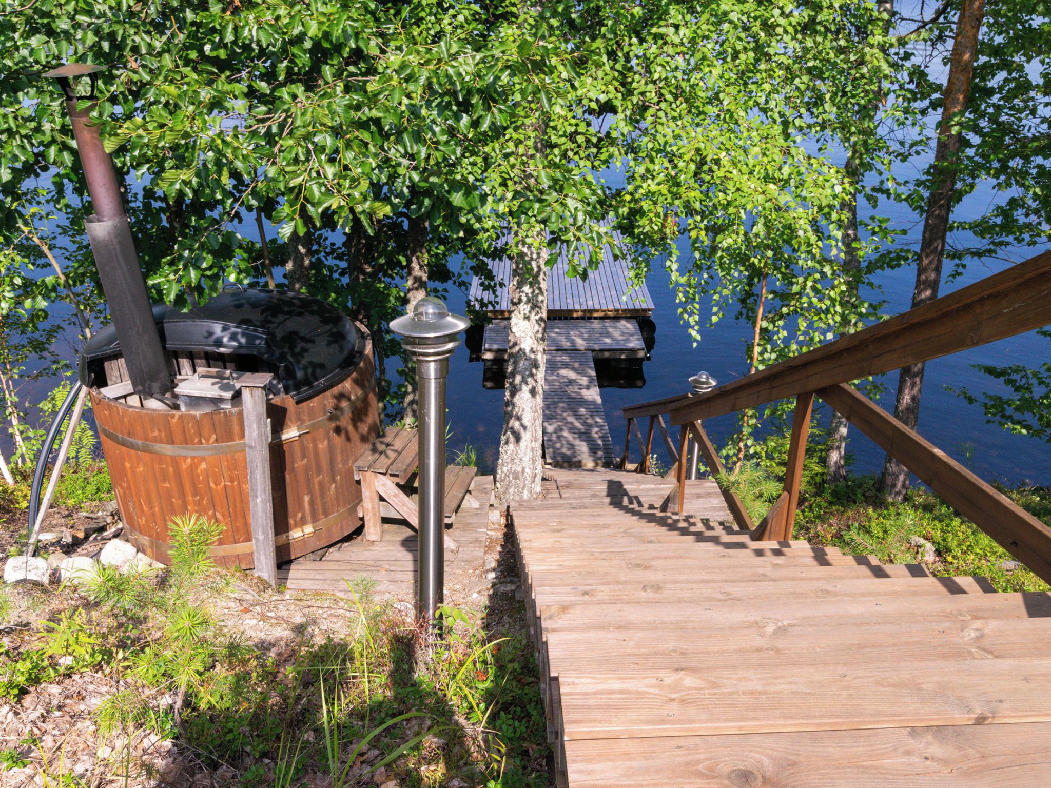 A wooden deck leading to a dock, a hot tub, and a chimney.