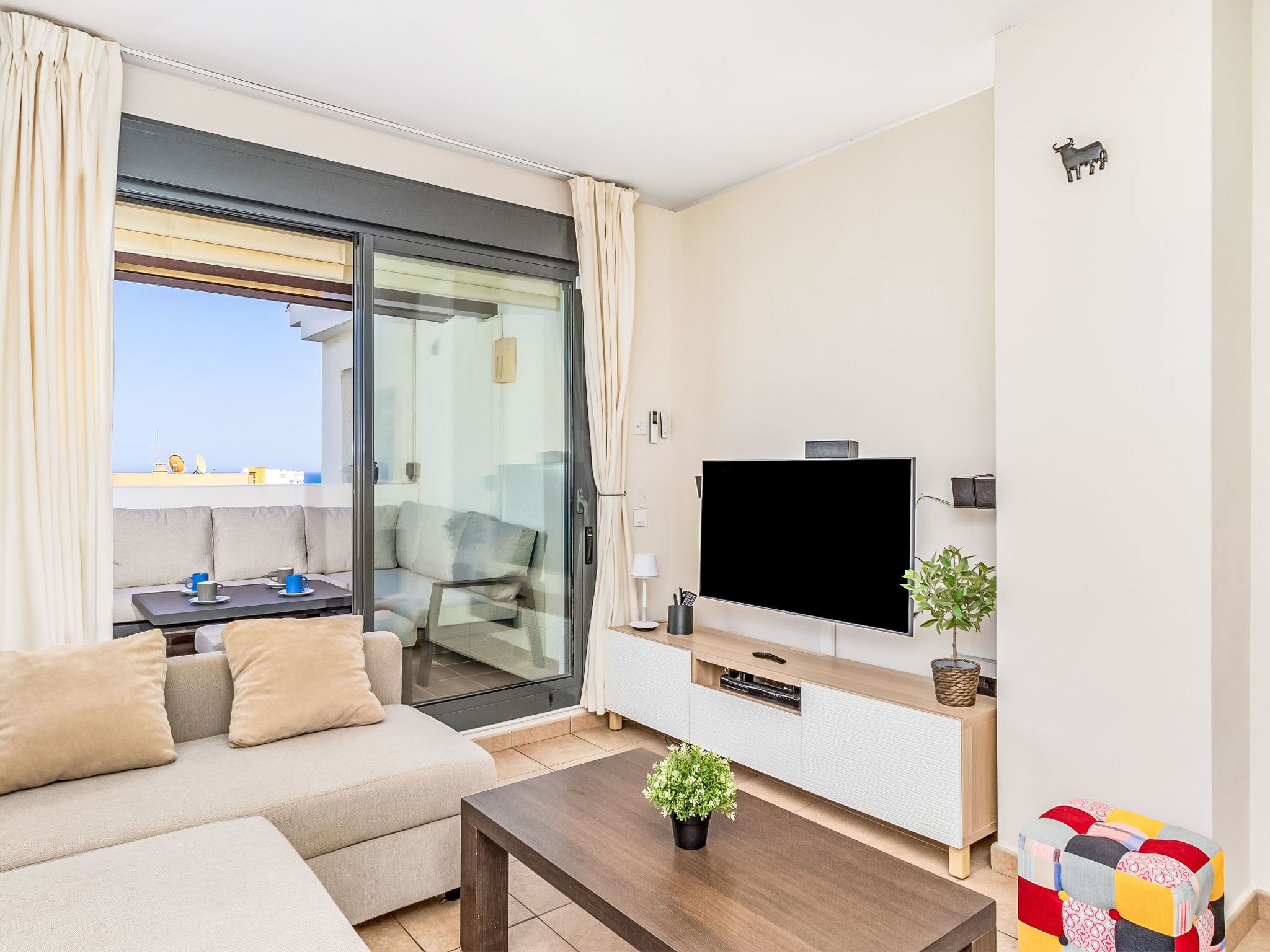 Una sala moderna con sofá, mesa de centro, televisor y un balcón con vistas.