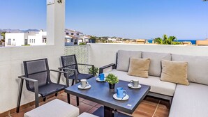 Eine Dachterrasse mit einer Couch, Stühlen, einem Tisch und Blick auf das Meer und die Gebäude.