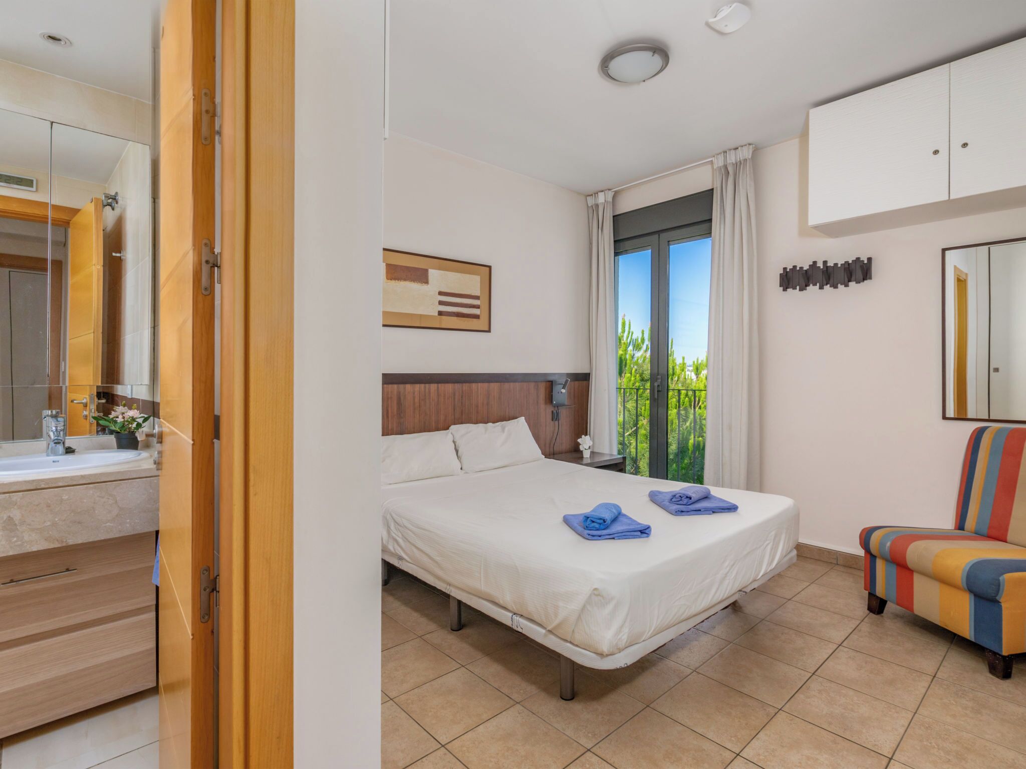 Una habitación de hotel con cama, baño, ventana con cortinas y una silla colorida.