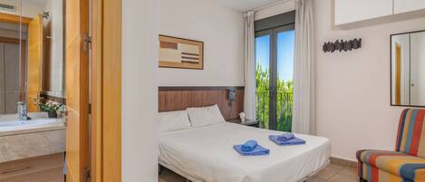 Una habitación de hotel con cama, baño, ventana con cortinas y una silla colorida.