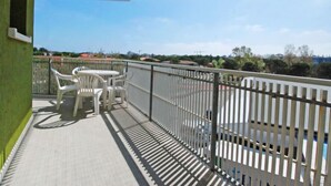 Een balkon met een witte tafel en stoelen, een metalen hekwerk en uitzicht op gebouwen en bomen.