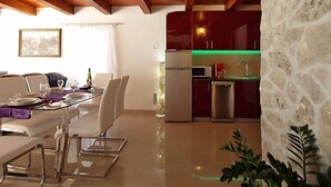 Un coin repas avec une table dressée pour quatre personnes, une cuisine équipée d’appareils modernes et un mur en pierre.