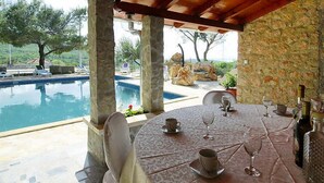 Un espace extérieur abrité, aménagé pour les repas, avec une piscine, des piliers en pierre et une vue sur le paysage.
