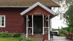 Een houten gebouw met een veranda en een bordje waarop 