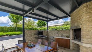 An outdoor patio with a stone wall, a grill, a sink, and a wooden table with chairs.