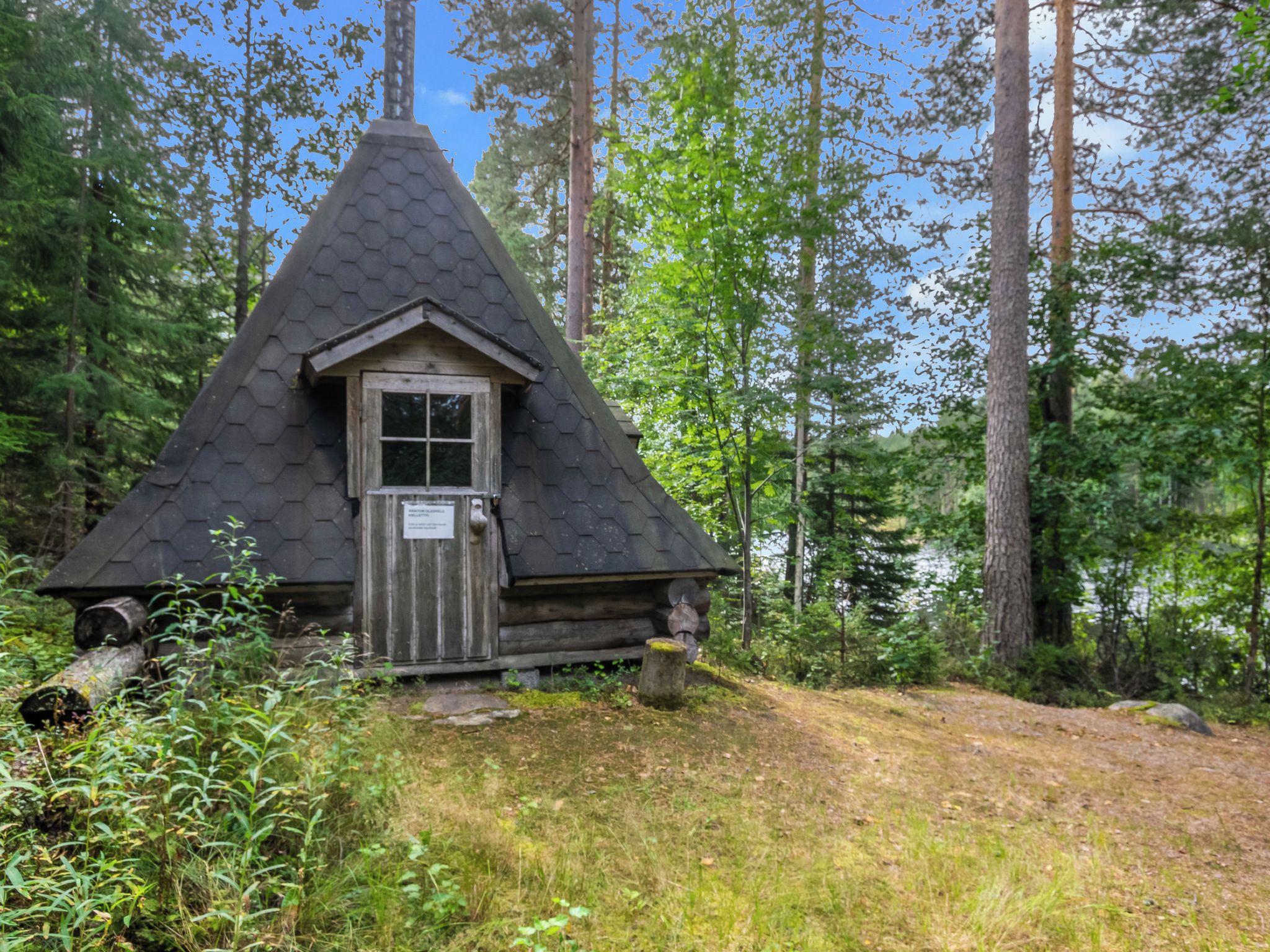 Eine kleine, sechseckig-gedeckte Holzhütte, umgeben von dichtem Wald.
