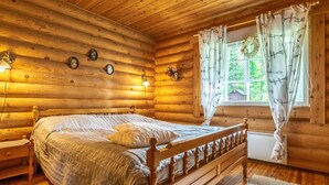 A log cabin room with a wooden bed, a nightstand, a window with curtains, and wall-mounted lights.